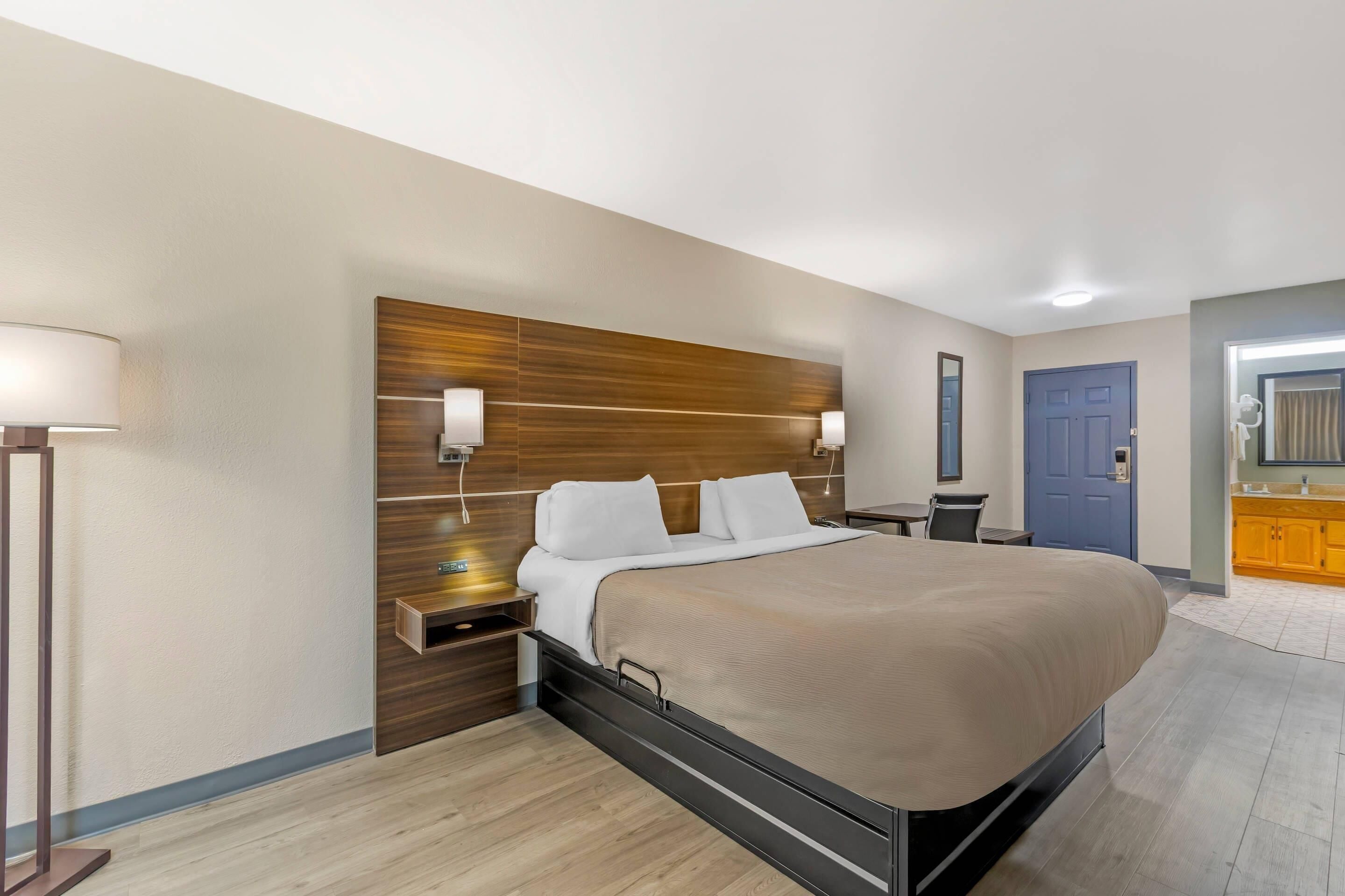 A modern hotel room with a large bed, wooden headboard, bedside lamps, and a small table.