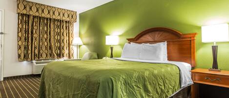 A hotel room with a green wall, a wooden headboard, a green bedspread, two bedside lamps, and a patterned curtain.