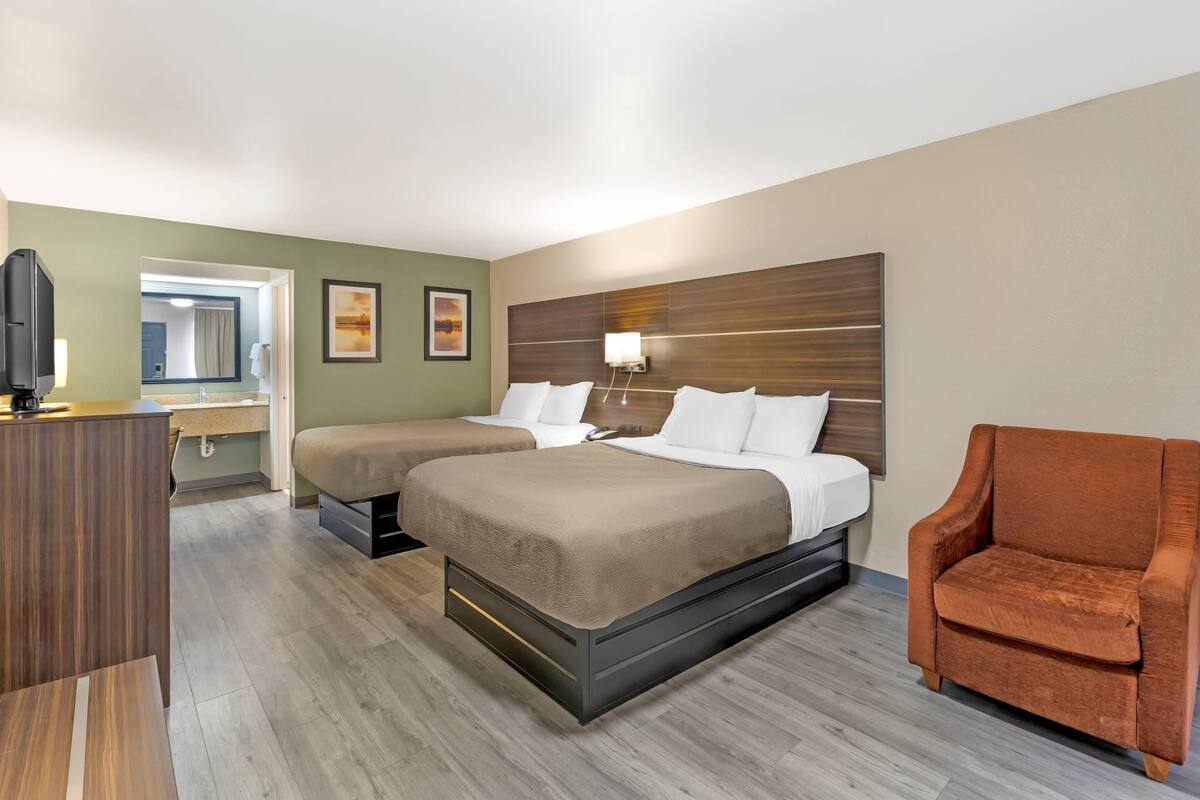 A hotel room with two beds, a TV, a desk, and a chair.