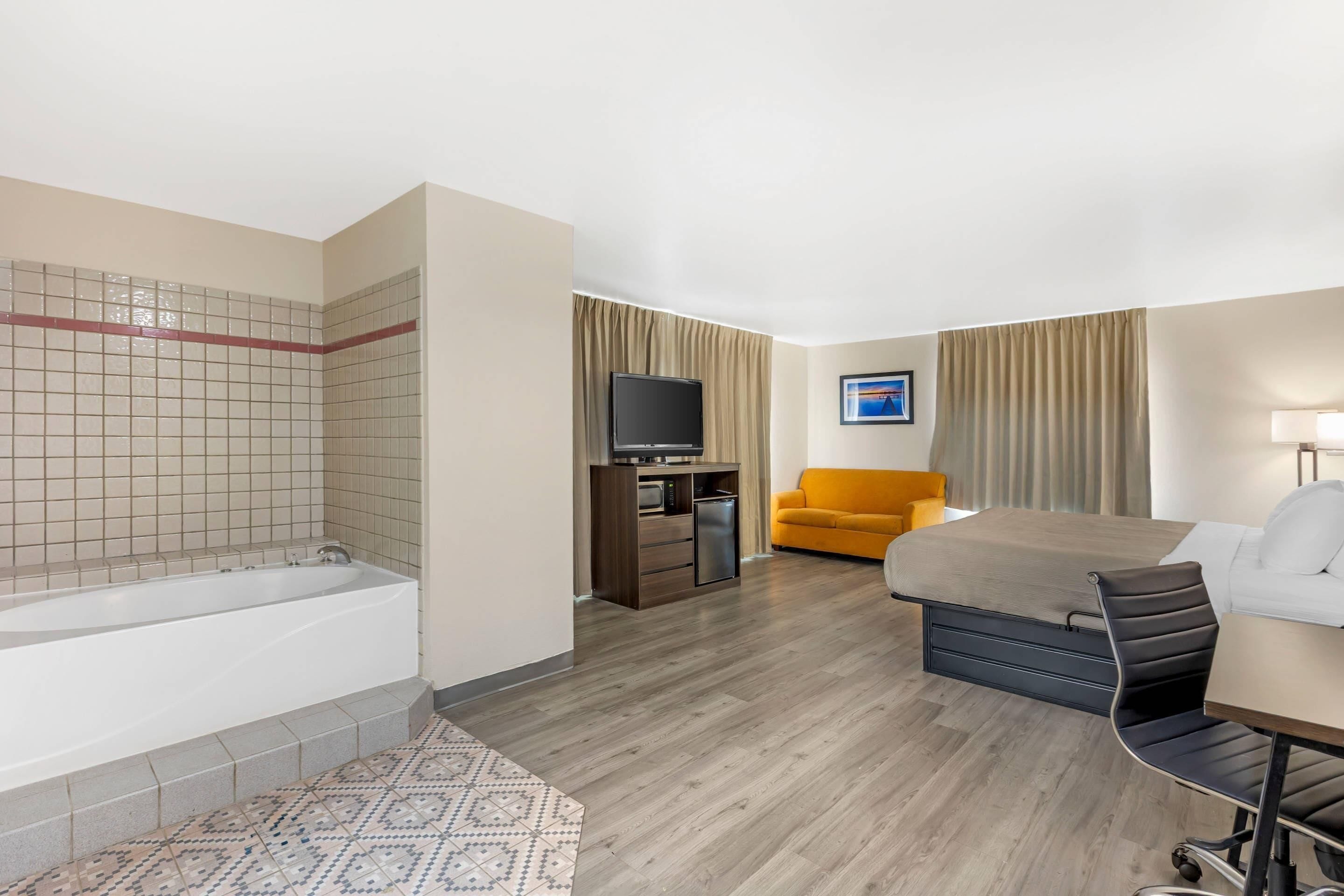 Habitación de hotel con bañera, sofá, escritorio y televisor.