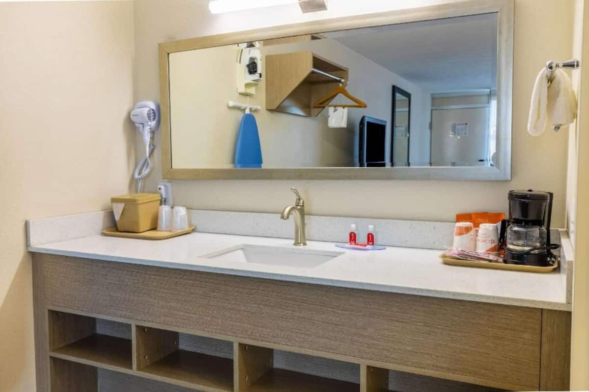 Ein Badezimmer mit Waschbecken, Spiegel, Haartrockner und Pflegeprodukten.