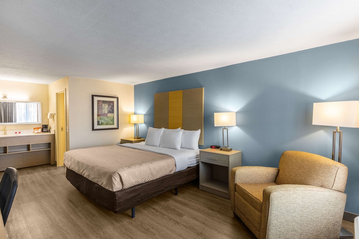 Ein Hotelzimmer mit Bett, Nachttischen, einem Sessel, einem Schreibtisch und einer Lampe.