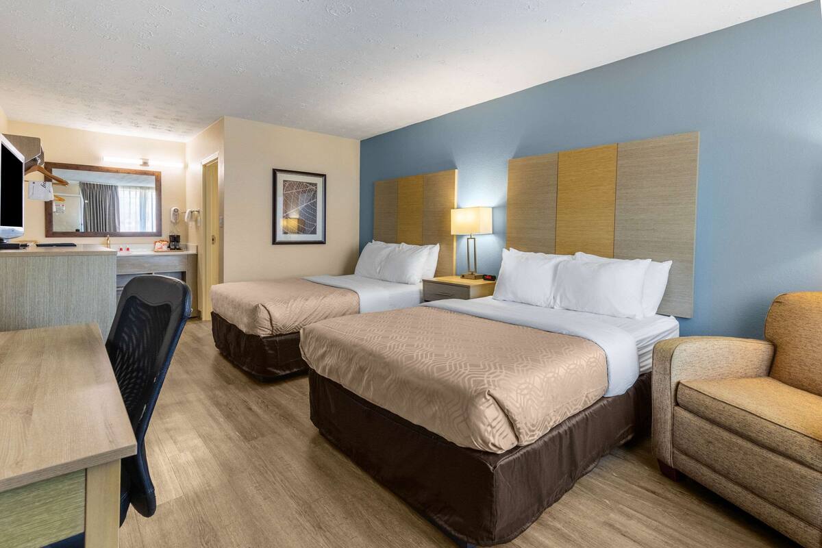Ein Hotelzimmer mit zwei Betten, einem Schreibtisch, einem Stuhl und einem Nachttisch mit Lampe.