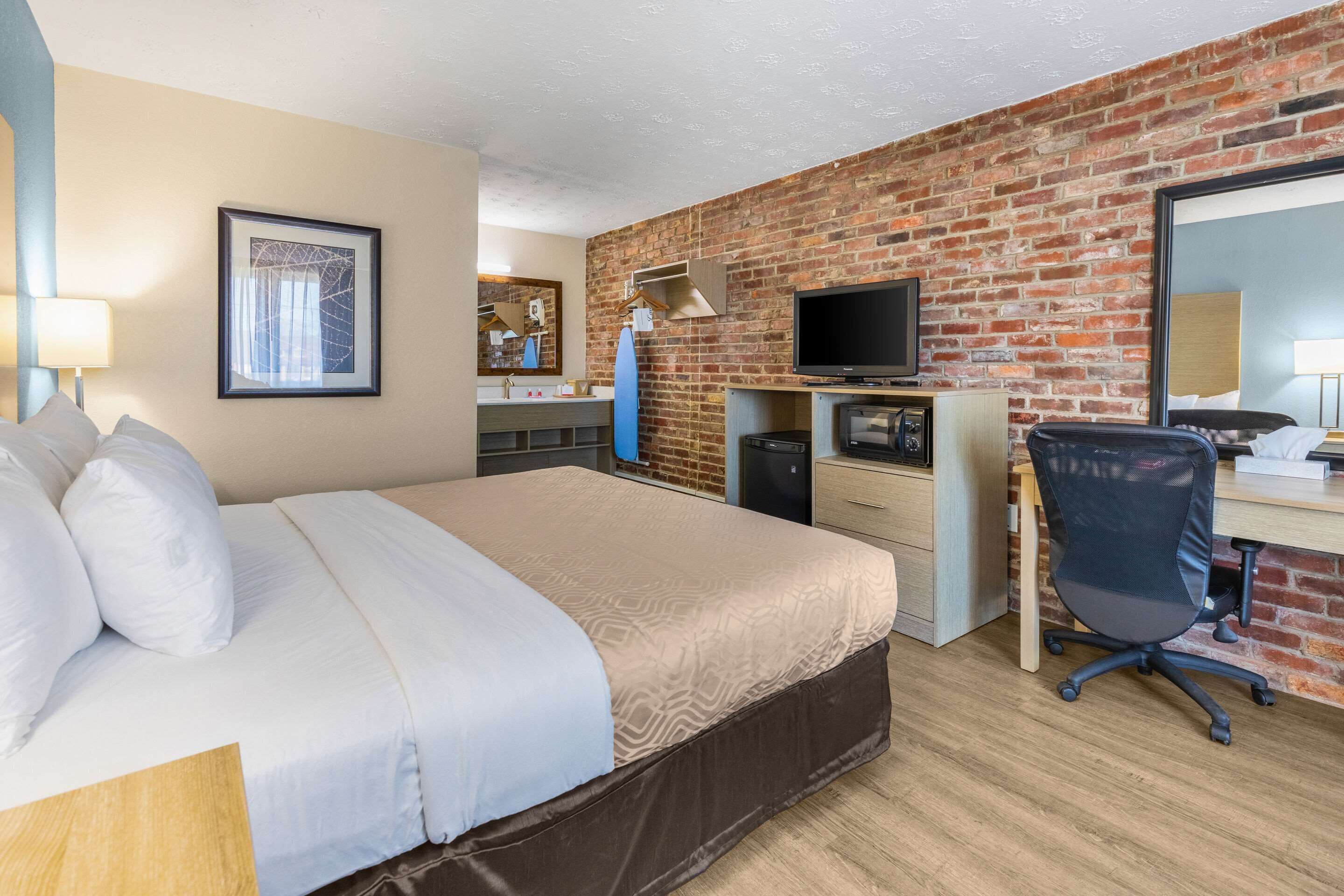 A hotel room with a bed, desk, TV, and a brick wall.