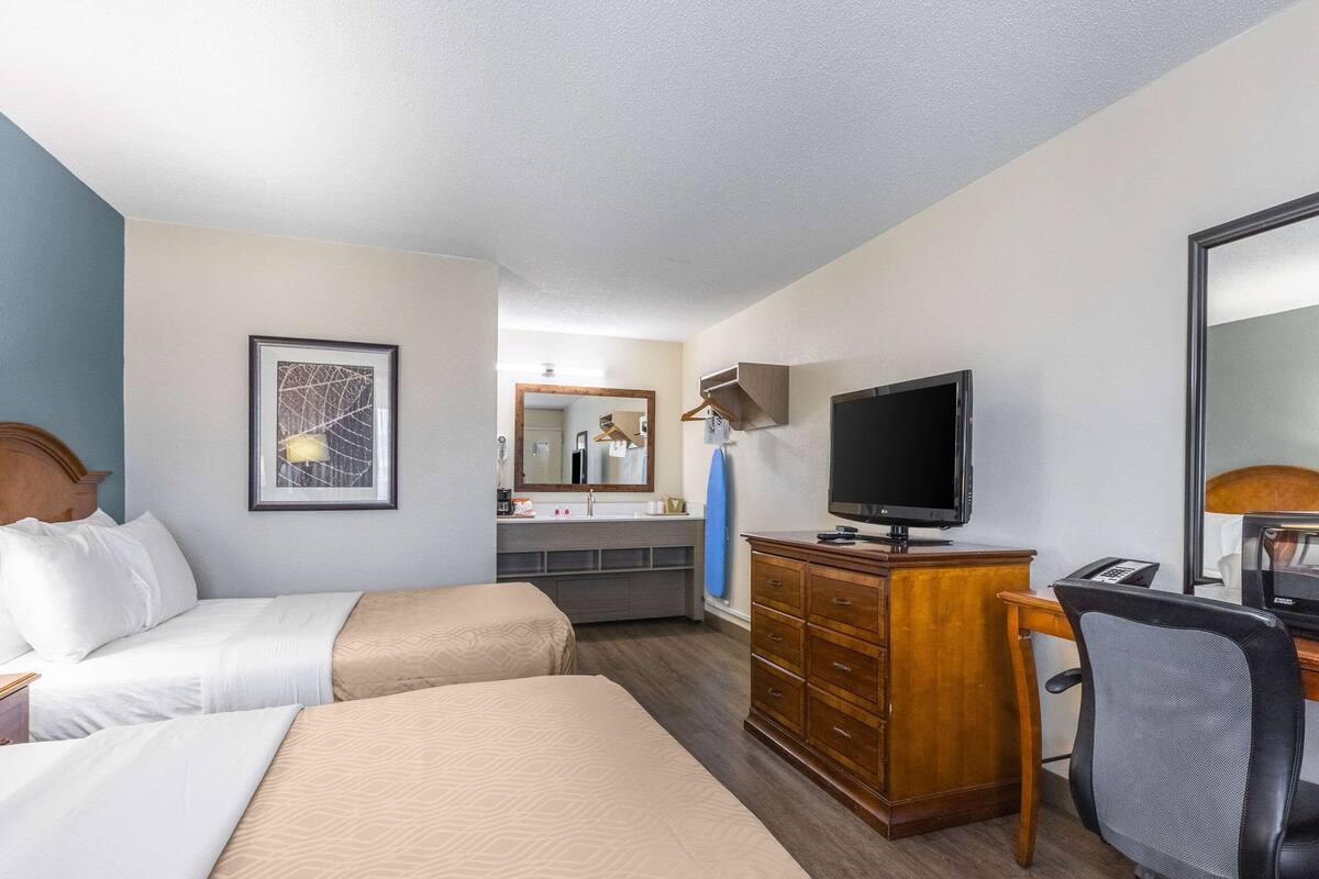 Ein Hotelzimmer mit zwei Betten, einem Schreibtisch, einem Fernseher, einem Schminktisch und einem Spiegel.
