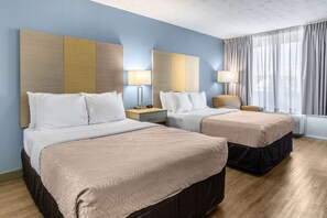 A hotel room with two beds, a nightstand, a lamp, and a window with curtains.