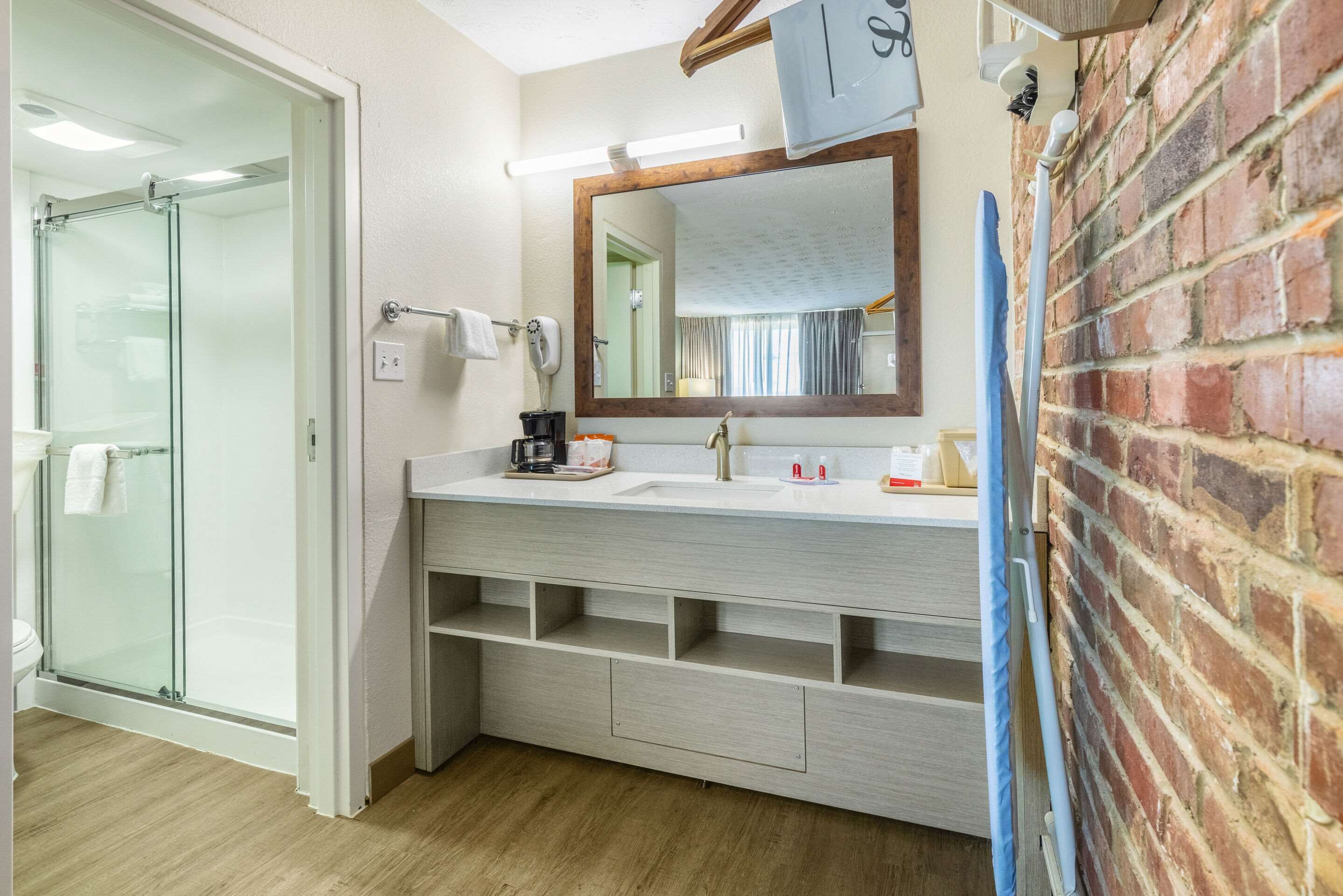 A modern bathroom with a glass shower enclosure, a white vanity with a mirror, and a brick accent wall.