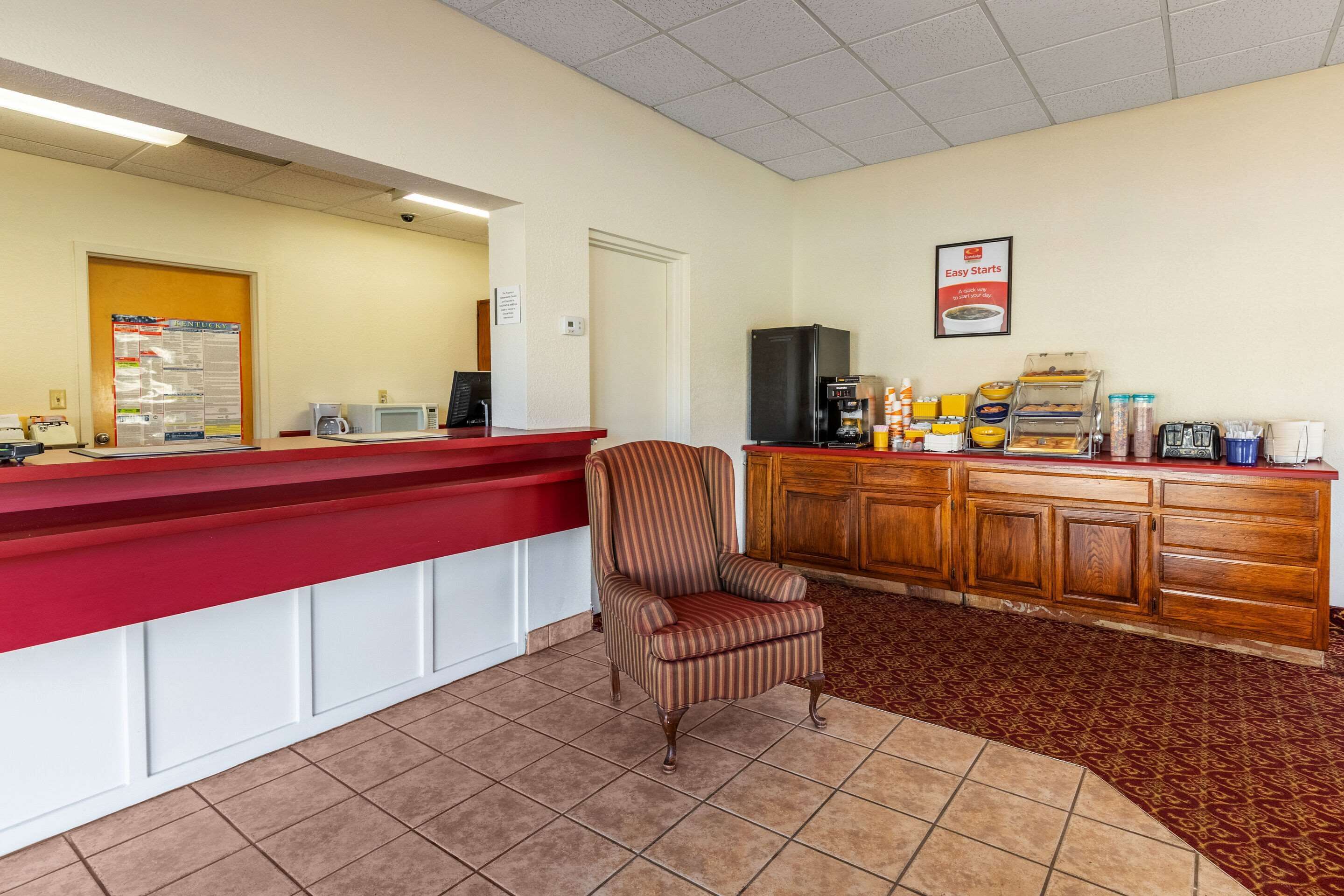 Una zona de recepción con un mostrador rojo, un sillón a rayas, una cafetera y un refrigerador.