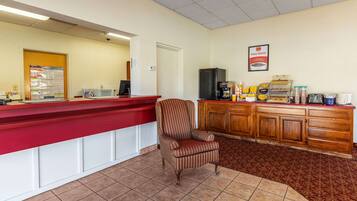 Una zona de recepción con un mostrador rojo, un sillón a rayas, una cafetera y un refrigerador.