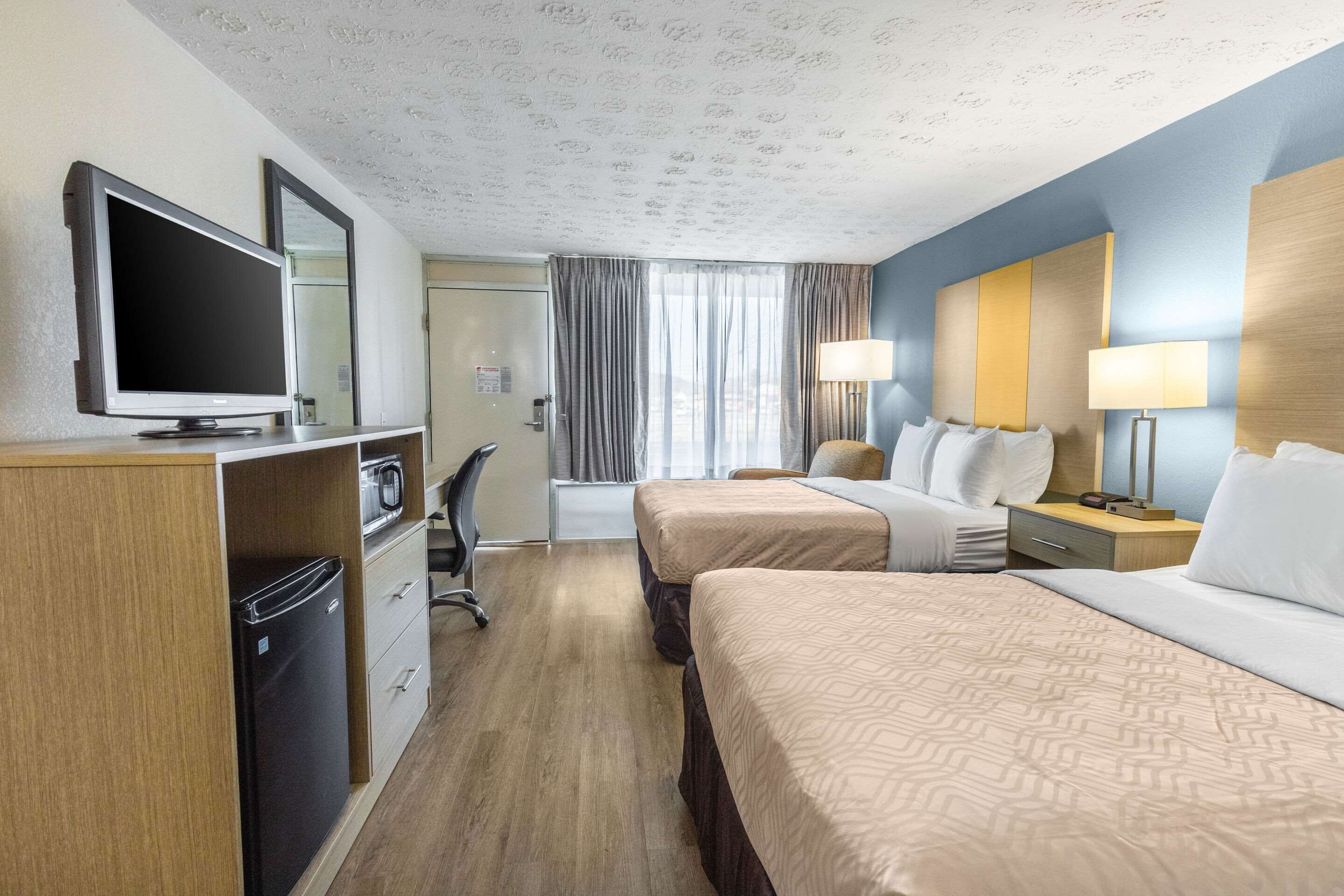 Habitación de hotel con dos camas, un escritorio, un televisor de pantalla plana, un refrigerador, un microondas y la puerta del baño.