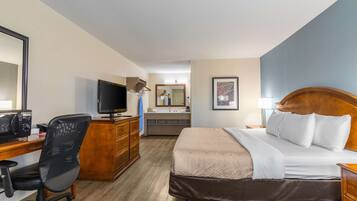 A hotel room with a bed, desk, chair, television, dresser, and a bathroom visible in the background.