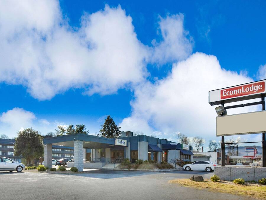 Un hotel con un letrero que dice 'Lobby', un estacionamiento y un cielo azul despejado con nubes.
