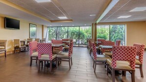 Un restaurant avec des banquettes et des tables, de grandes fenêtres et un téléviseur à écran plat fixé au mur.