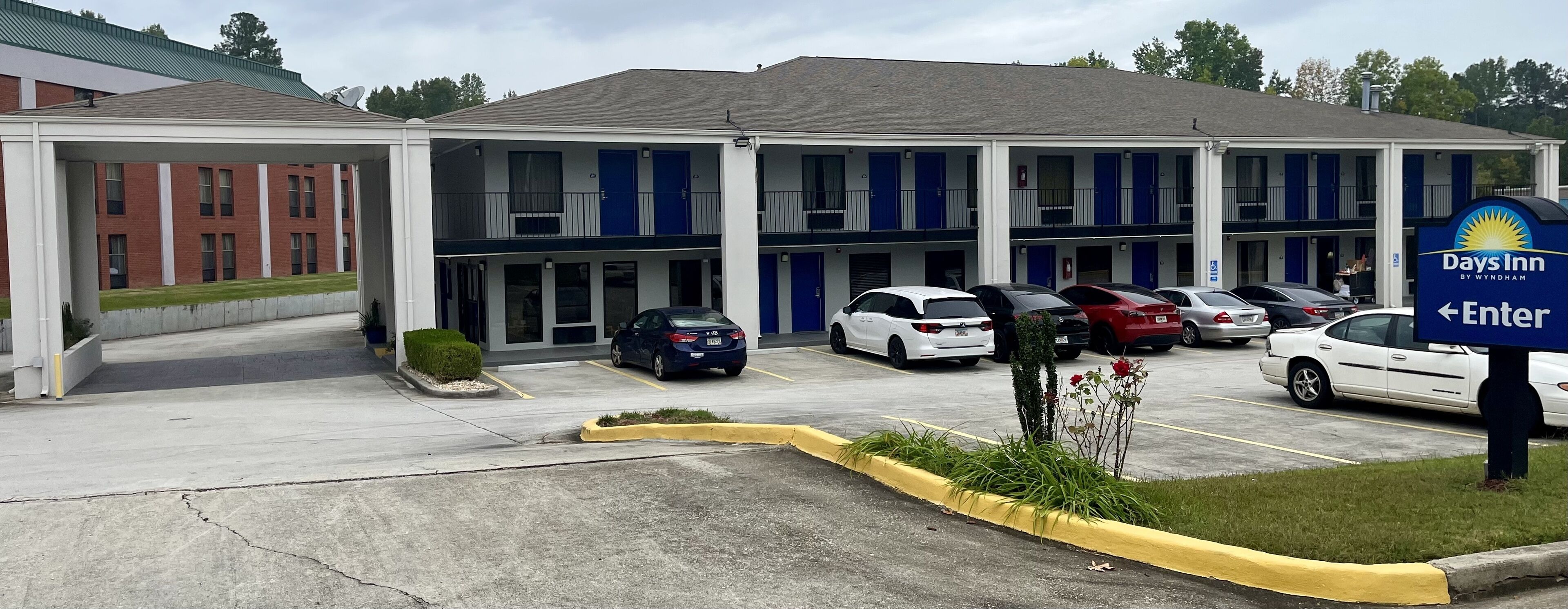 A Days Inn by Wyndham with a parking lot, a building with blue doors, and a sign indicating the entrance.