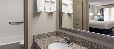 A hotel bathroom with a granite countertop sink, a mirror, and a towel rack.