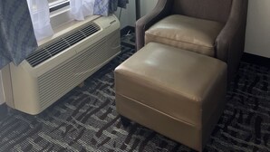Ett hotellrum med ett fönster, en luftkonditioneringsanläggning, en lampa och en brun läderfåtölj.