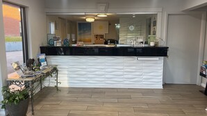 Ett receptionsområde med en svart receptionsdisk, en vit, strukturerad bakgrund och ett trägolv.