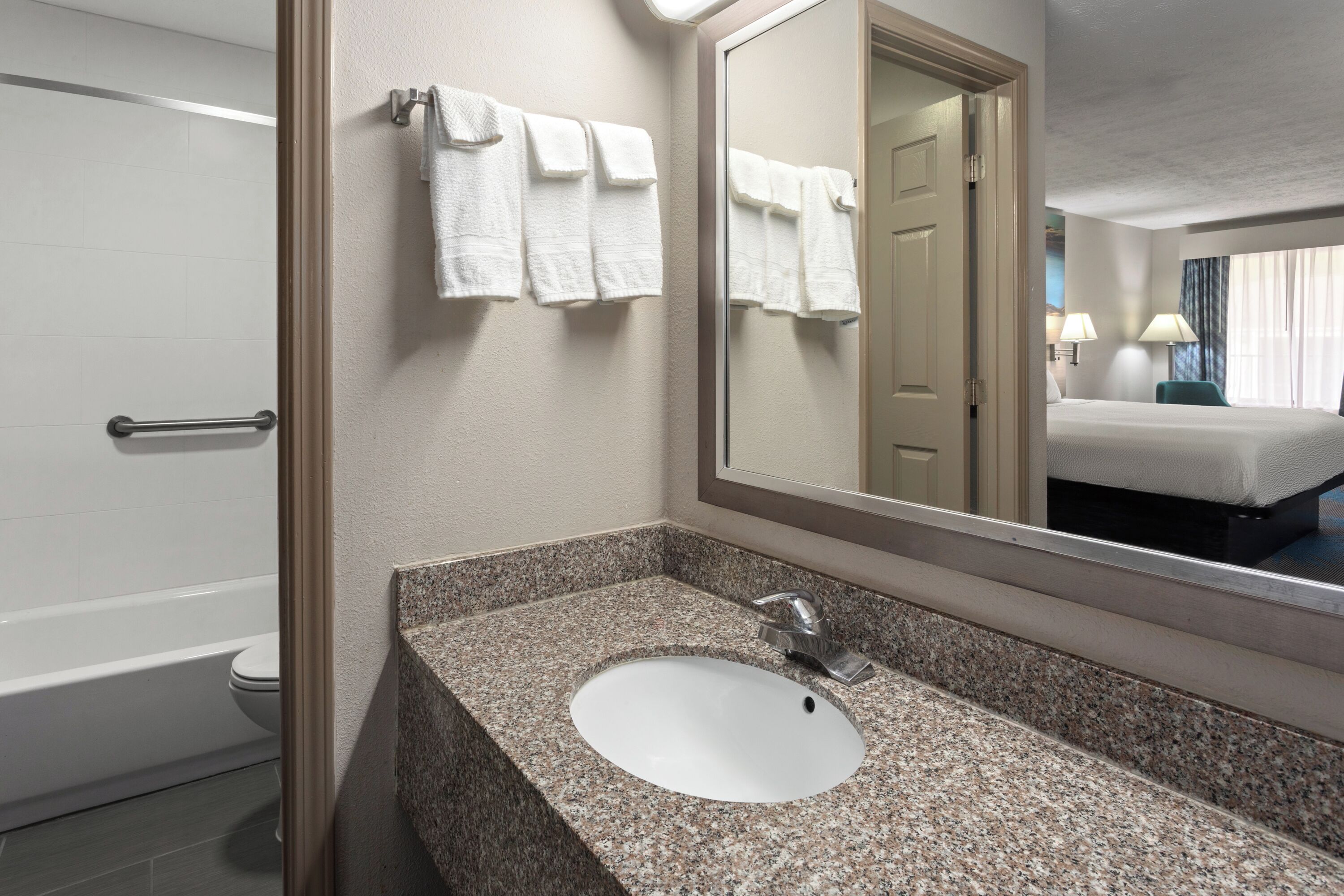 A bathroom with a granite countertop sink, a mirror, and a towel rack.