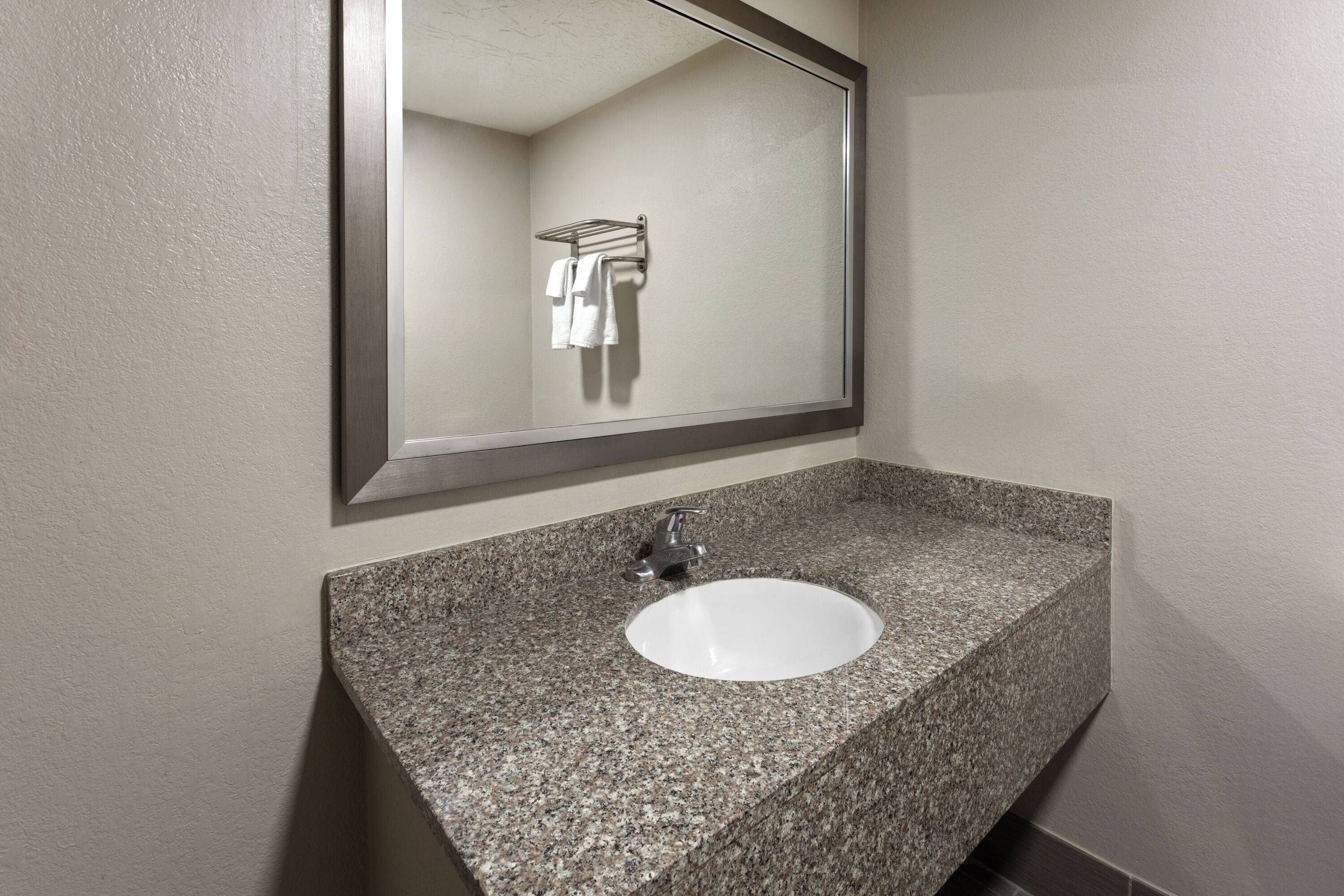 A bathroom with a granite countertop, a white sink, and a mirror.