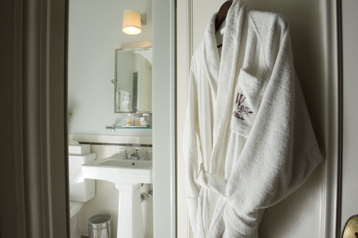 A bathroom with a white sink, mirror, and a robe hanging on the wall.