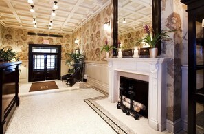 A lobby with a fireplace, patterned wallpaper, and a reception desk. - Hotel Wales (New York)
