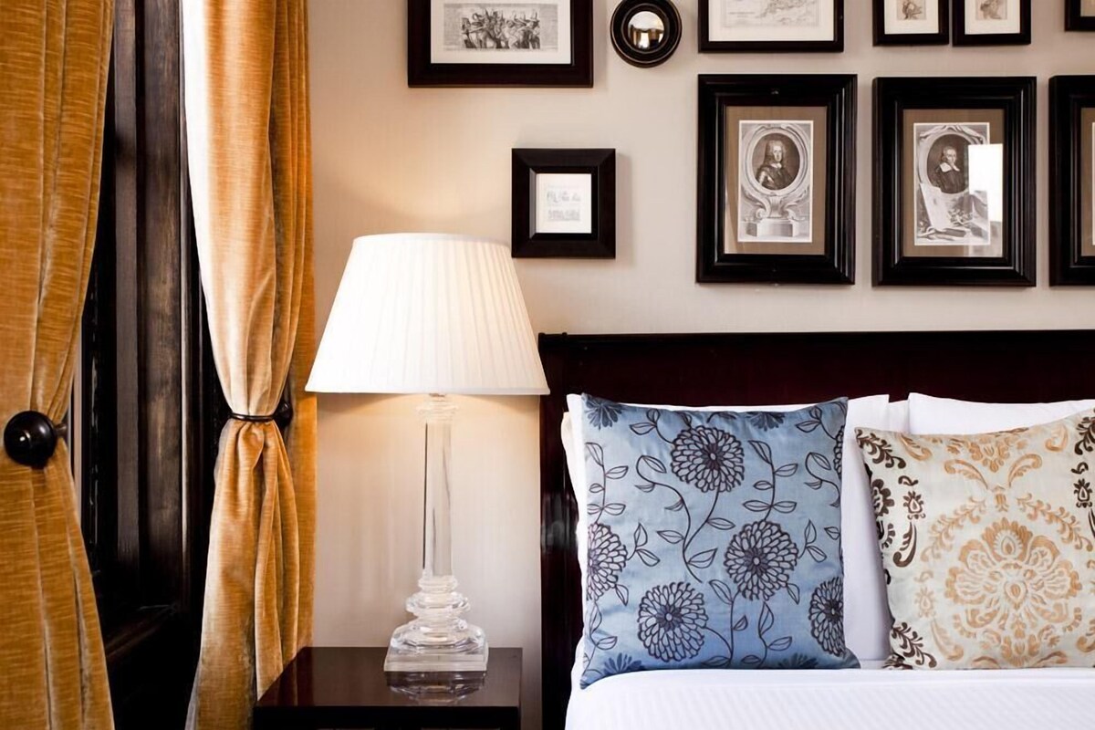A hotel room with a bed, a nightstand with a lamp, and a wall decorated with framed pictures.