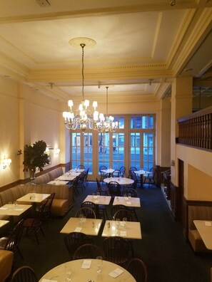 A dining area with tables and chairs, a chandelier, and a large window with a view. - Hotel Wales (New York)