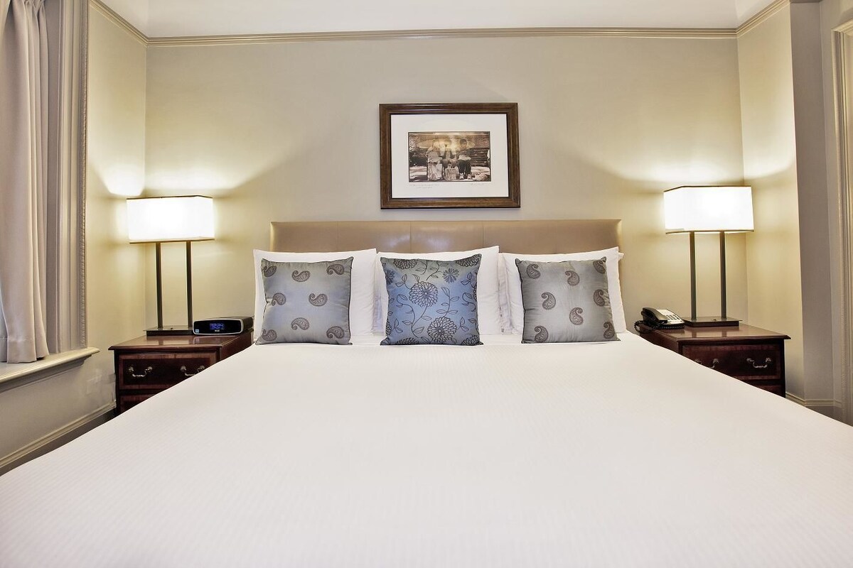 A hotel room with a large bed, two bedside tables, and two lamps.