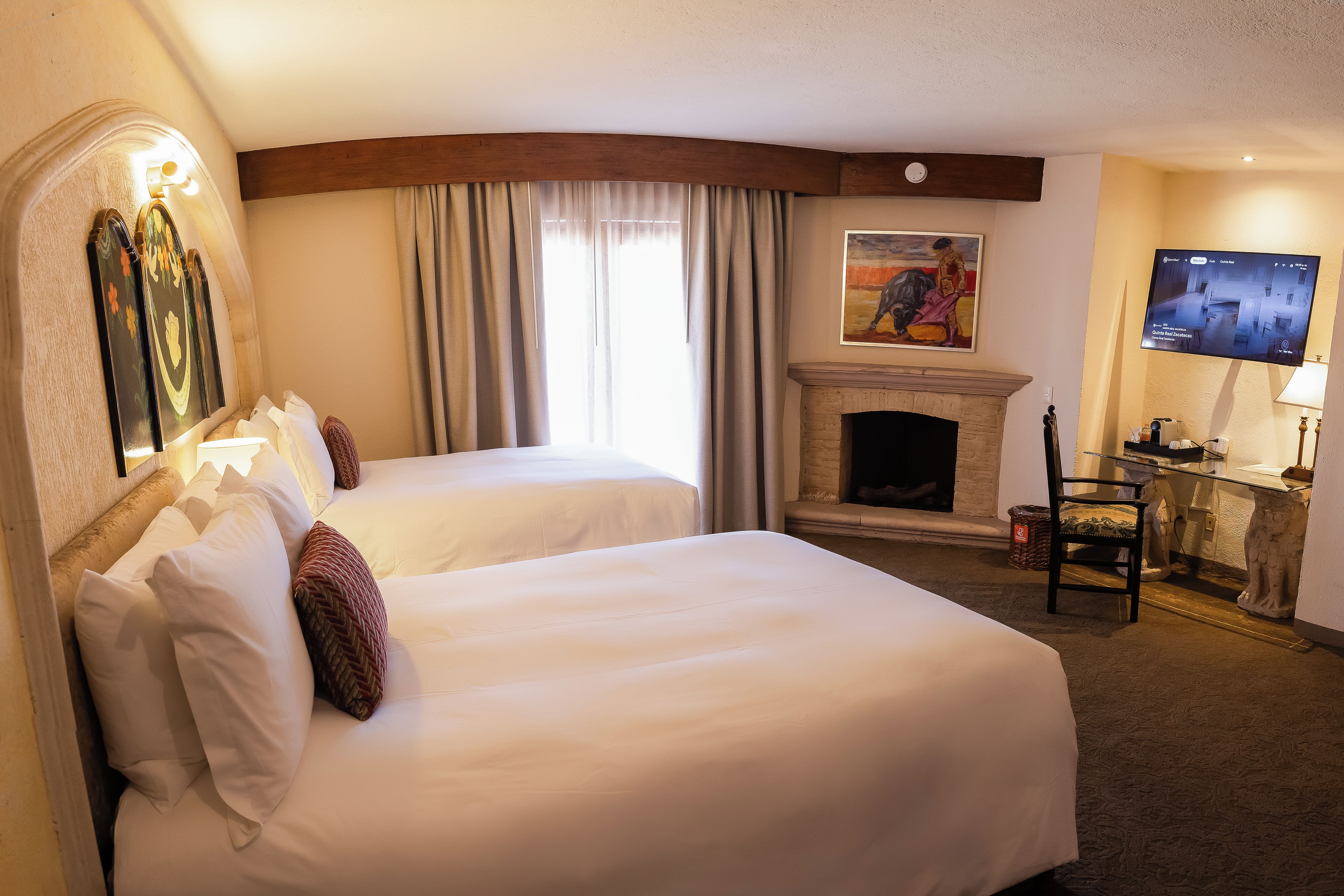 A hotel room with two beds, a fireplace, a television, and a desk with a chair.