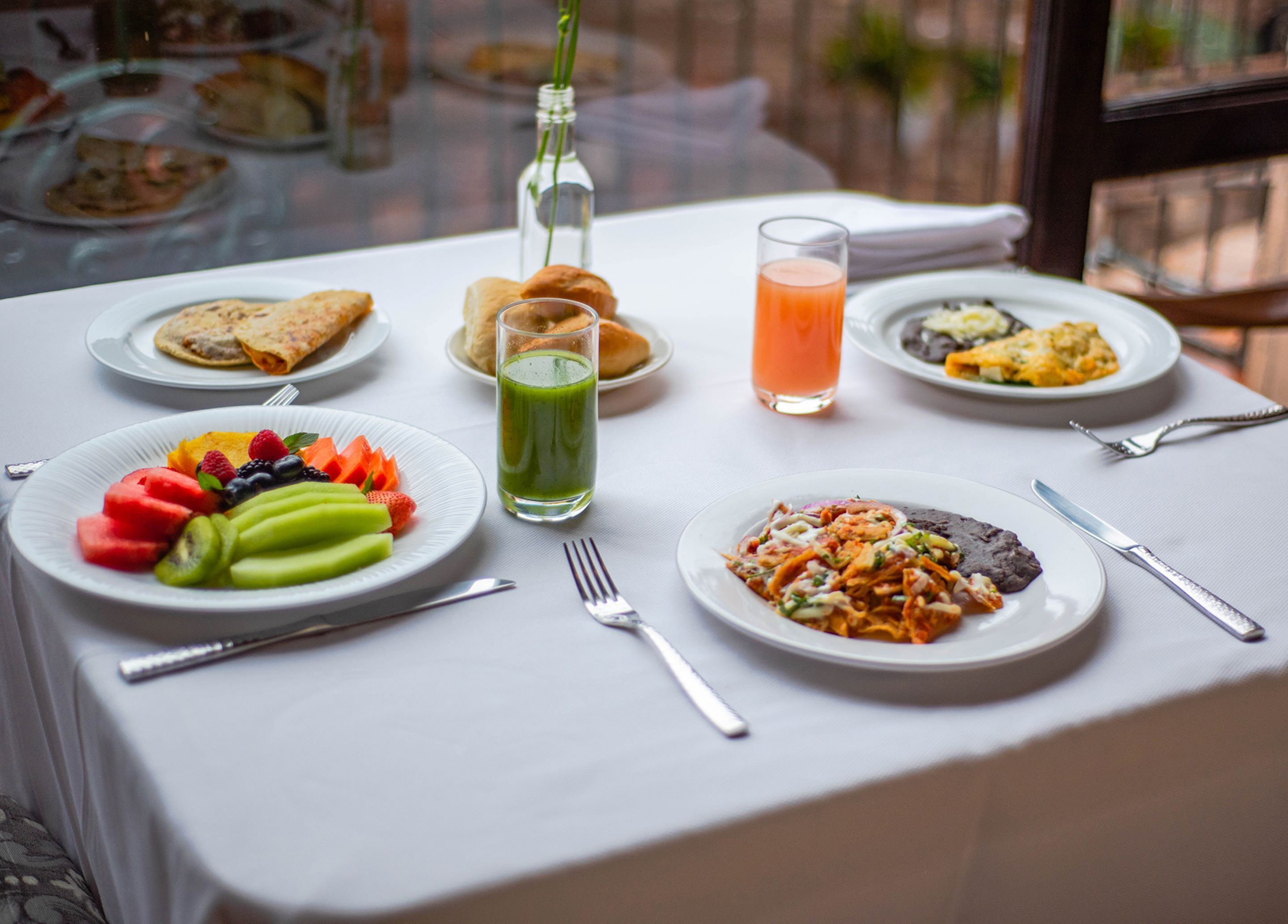 A breakfast table with plates of food, a glass of juice, and a bottle.