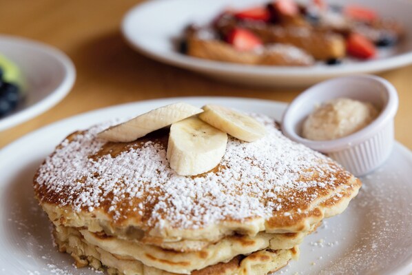 A stack of pancakes with bananas and powdered sugar on a plate.