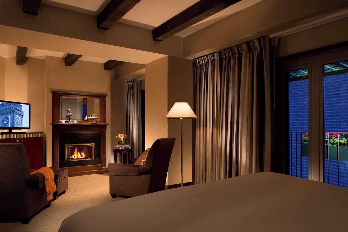 A hotel room with a fireplace, a television, a bed, a chair, and a balcony with a view.