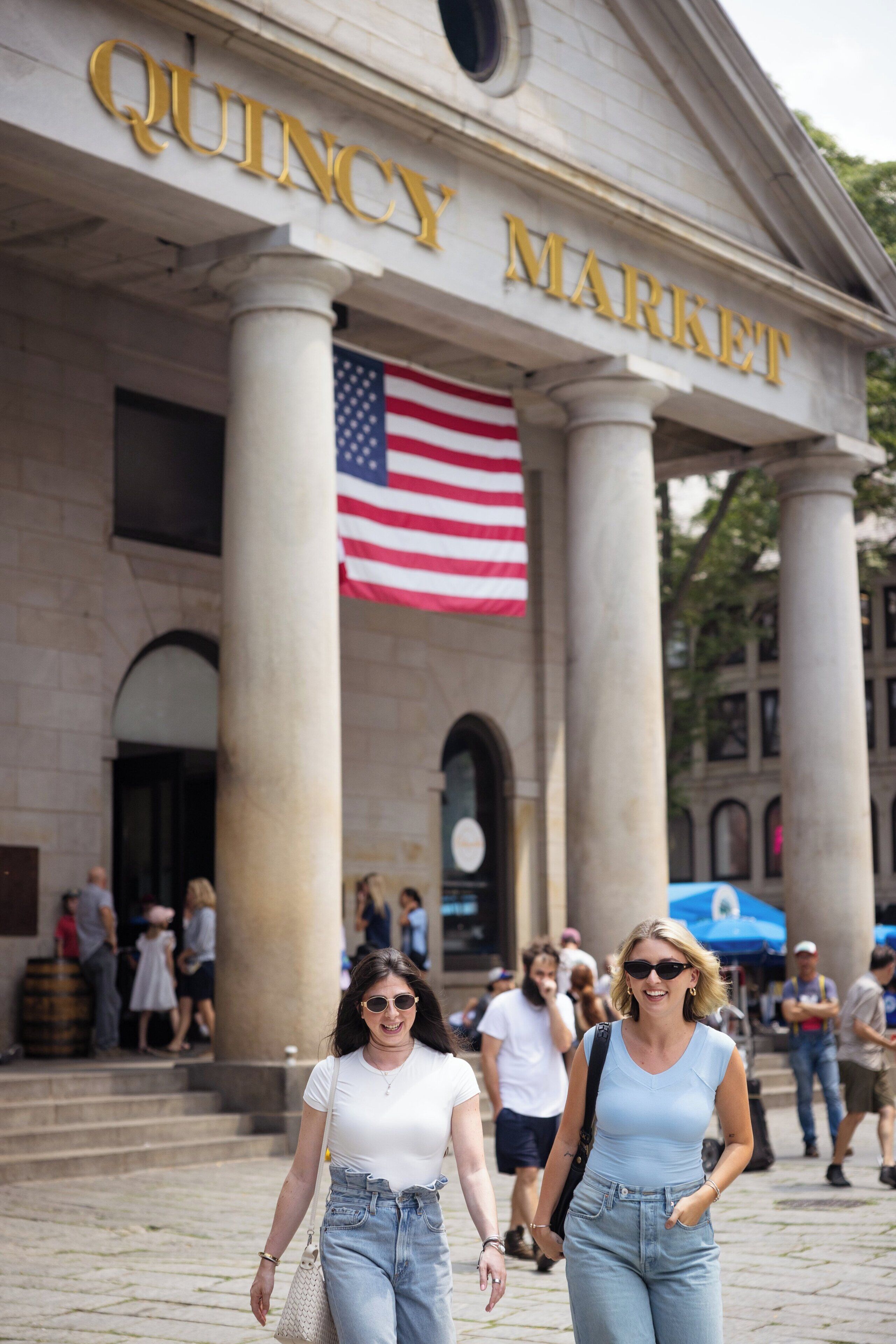 Un edificio con la inscripción 'QUINCY MARKET', grandes columnas y una bandera estadounidense.