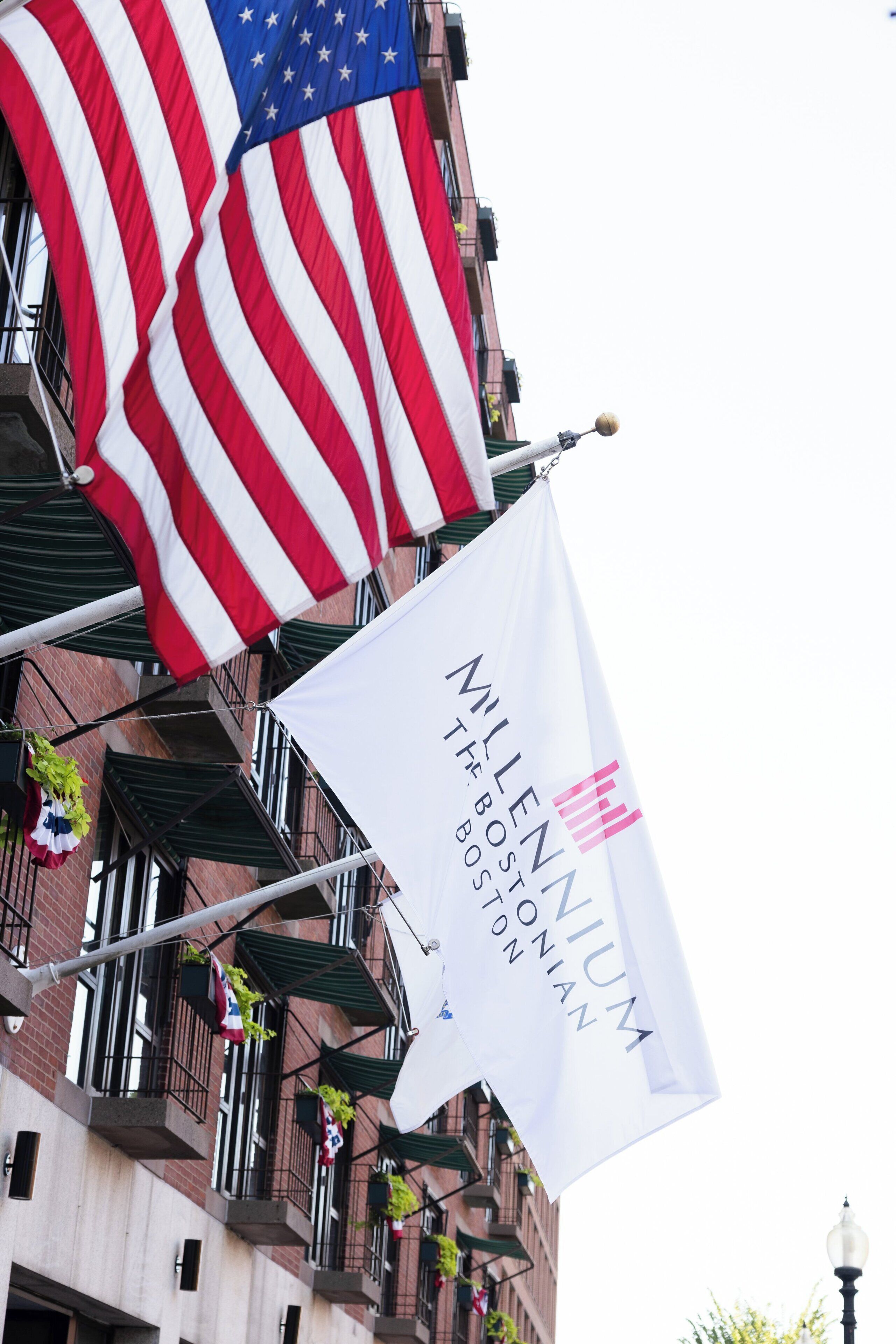 A building with multiple balconies, American flags, and a banner for Millenium The Bostonian.