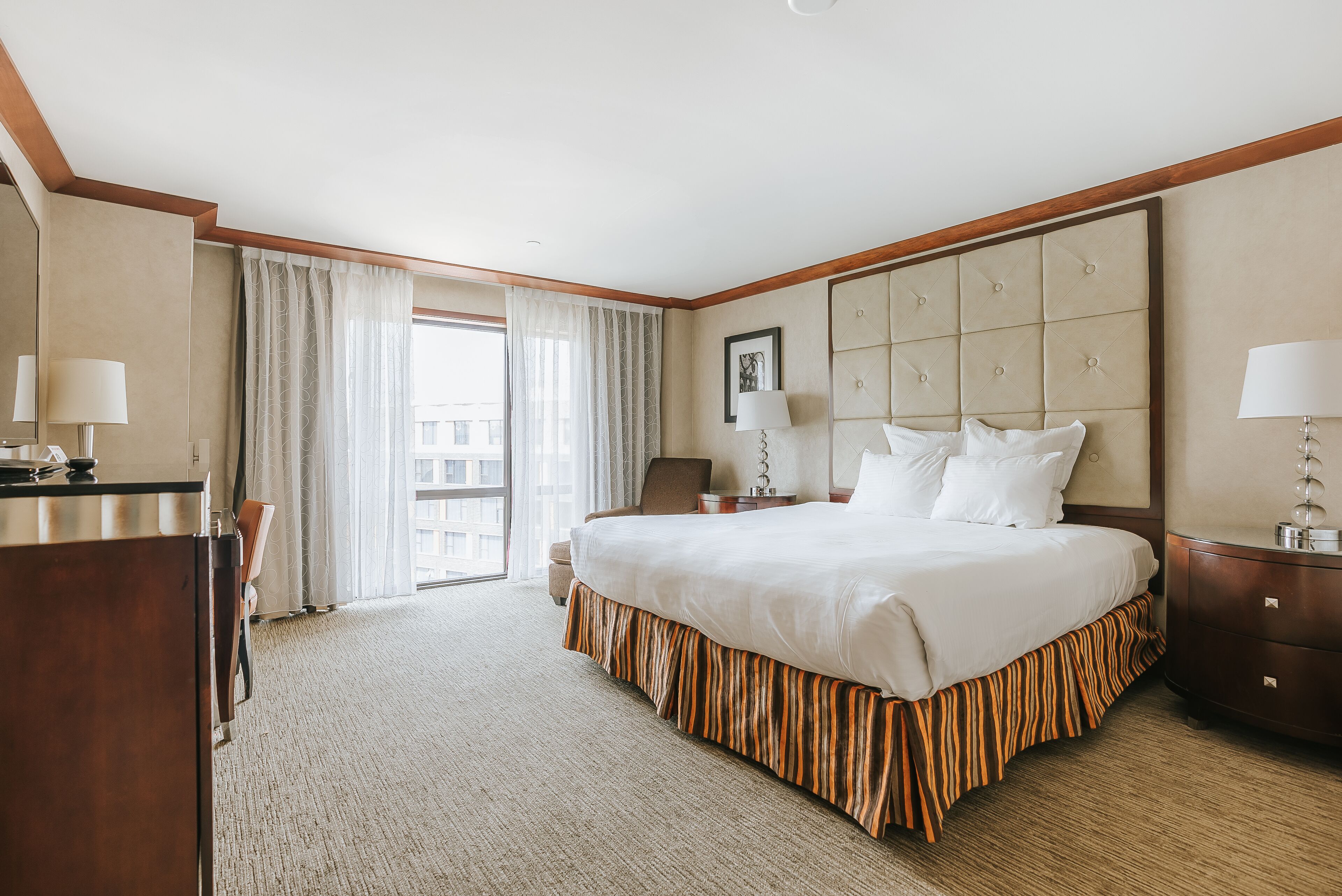 A hotel room with a large bed, a desk, a chair, and a window with curtains.