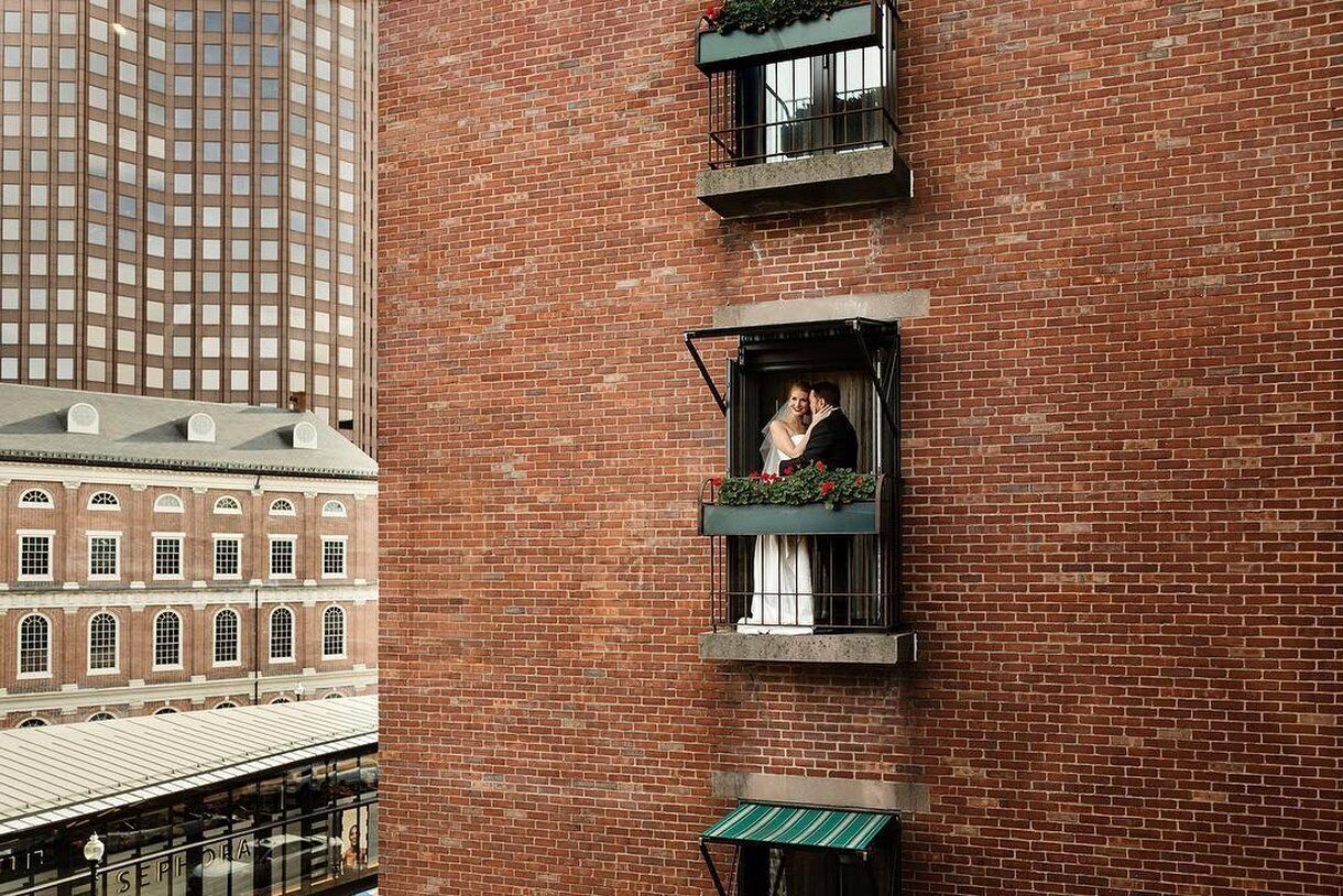 A brick building with a balcony where a couple is kissing.