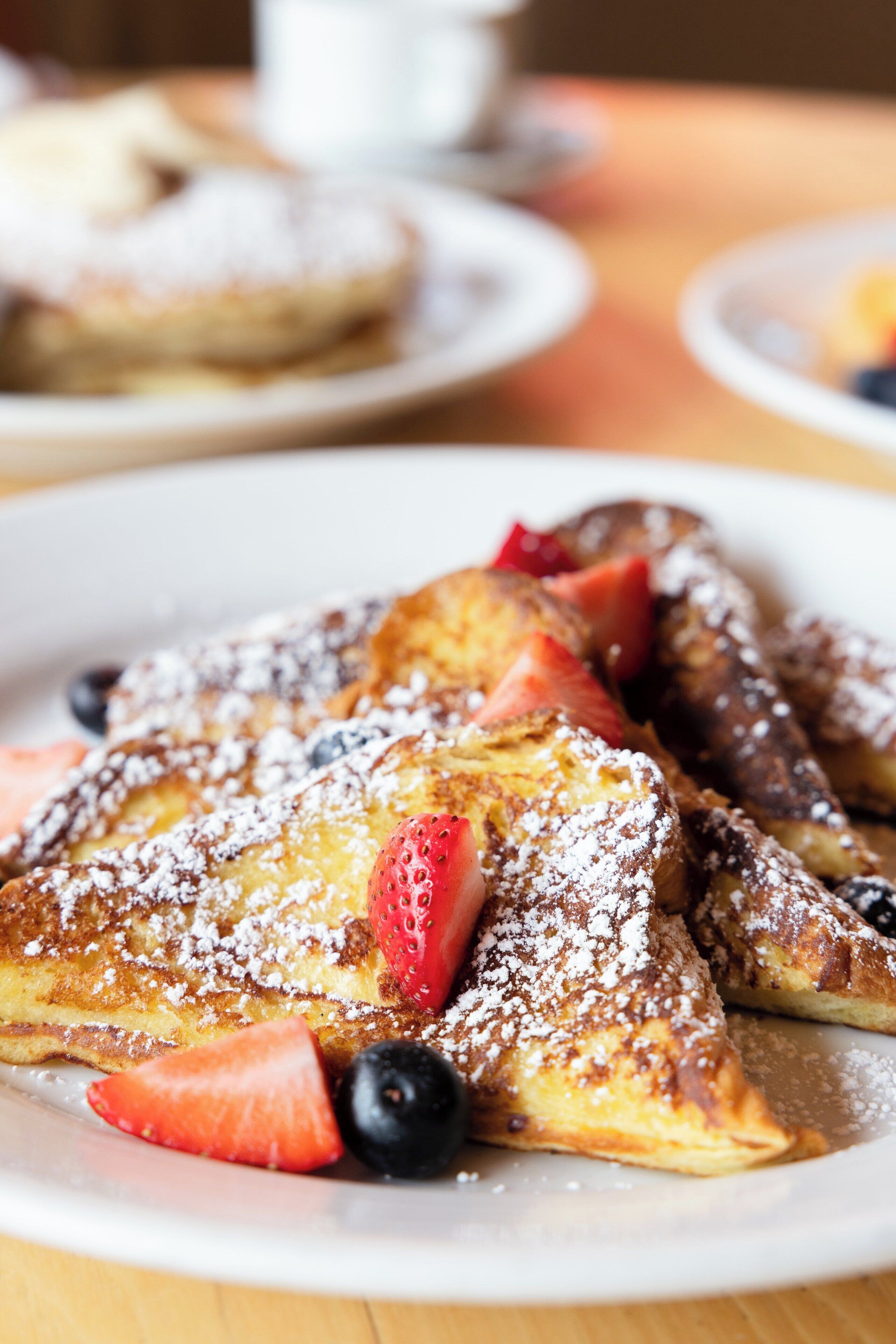 A plate of French toast with strawberries and blueberries, dusted with powdered sugar.