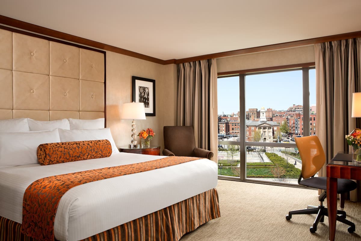 A hotel room with a large bed, a desk, a chair, and a view of the city.