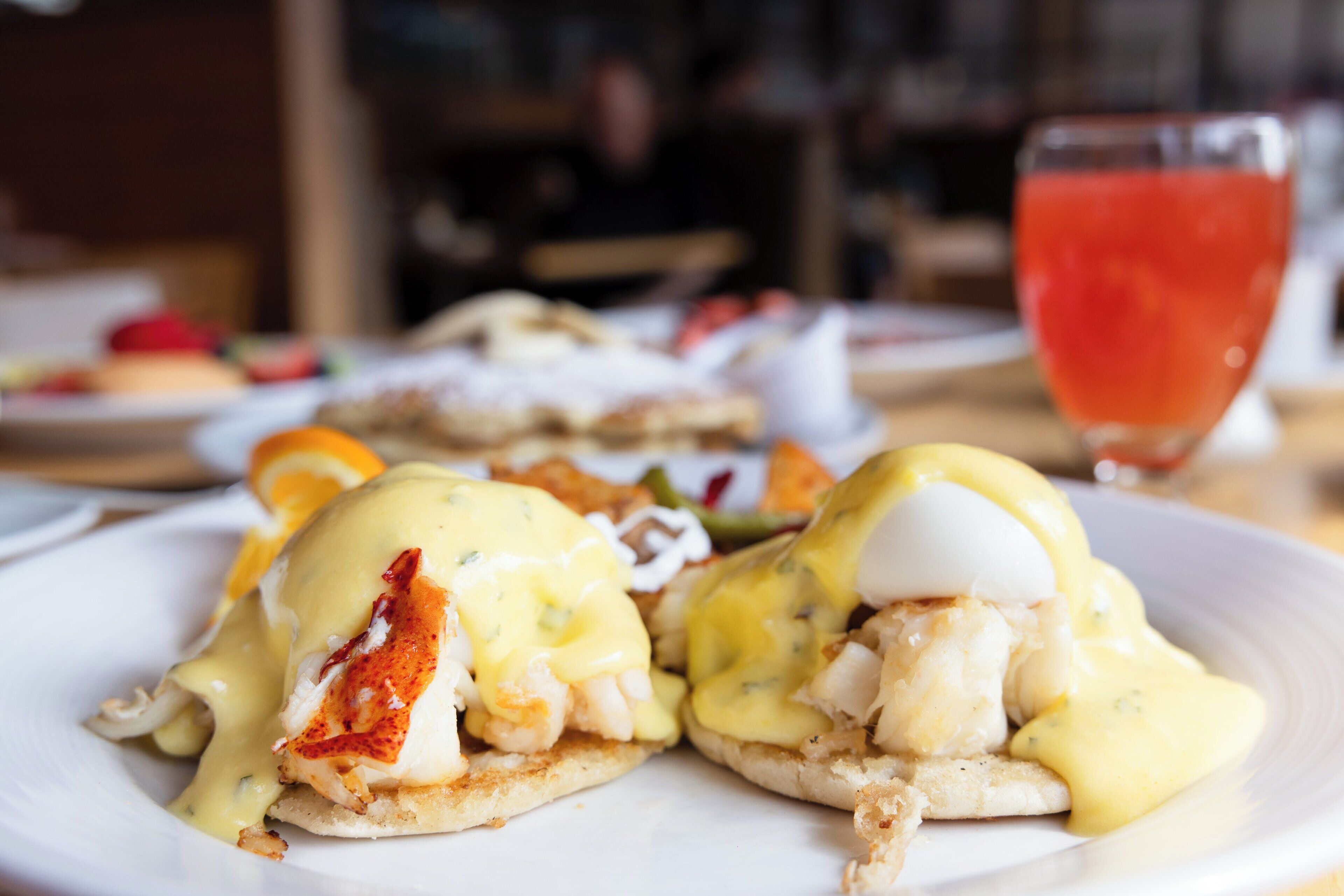 Ein Teller Eier Benedict mit Sauce Hollandaise und ein Glas roter Saft.