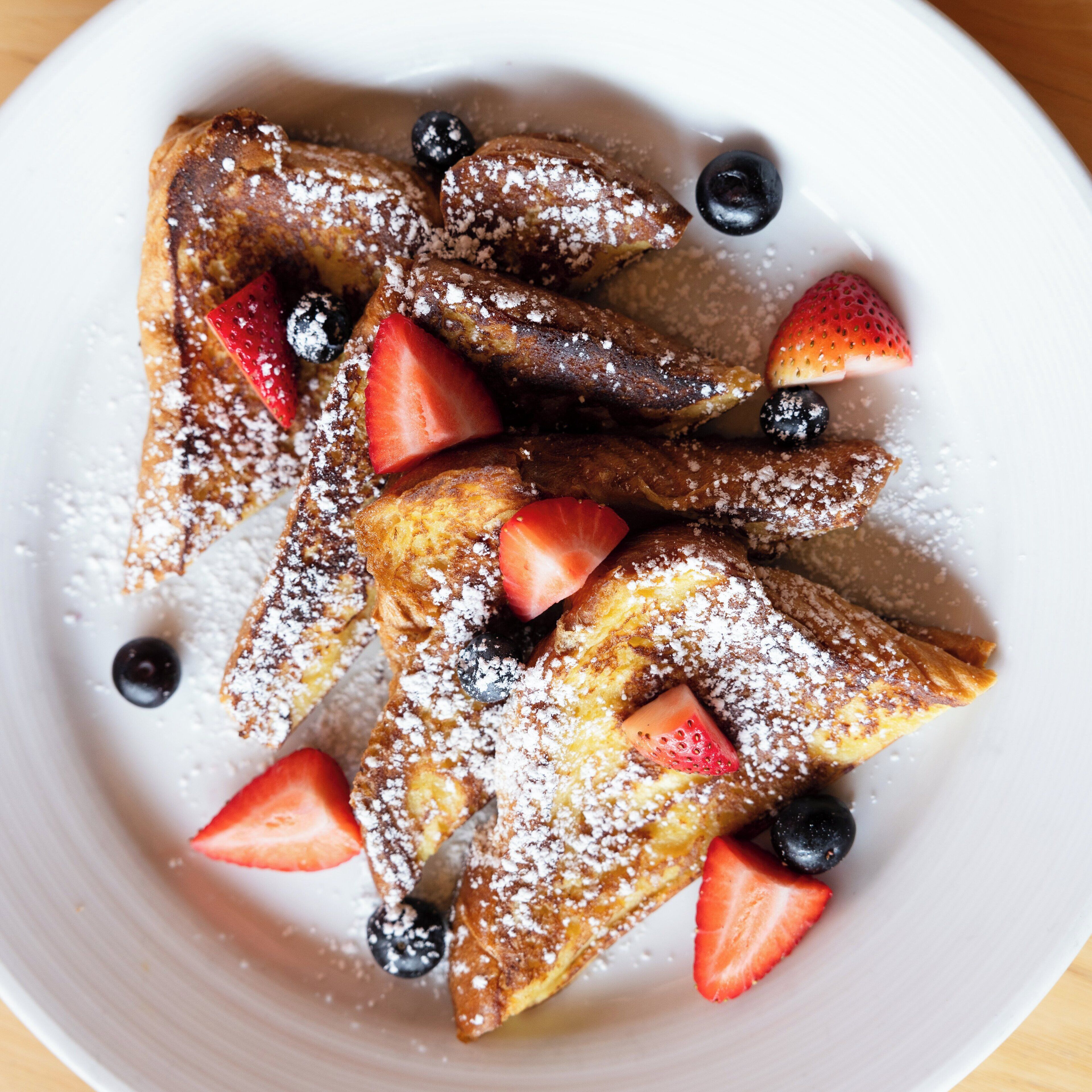 Un plato de tostadas francesas con fresas y arándanos, espolvoreadas con azúcar glass.