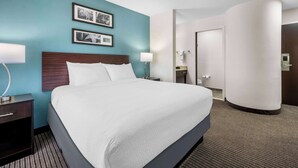 A hotel room with a large bed, a nightstand with a lamp, a wall-mounted picture, and a door leading to the bathroom. - Sleep Inn Springfield West (Springfield)