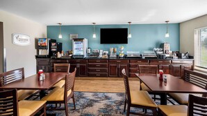 A hotel breakfast area with wooden tables and chairs, a flat-screen TV, and a refrigerator stocked with beverages and food items. - Sleep Inn Springfield West (Springfield)