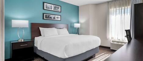 Una habitación de hotel con cama, mesitas de noche, lámparas y un ventanal con cortinas.