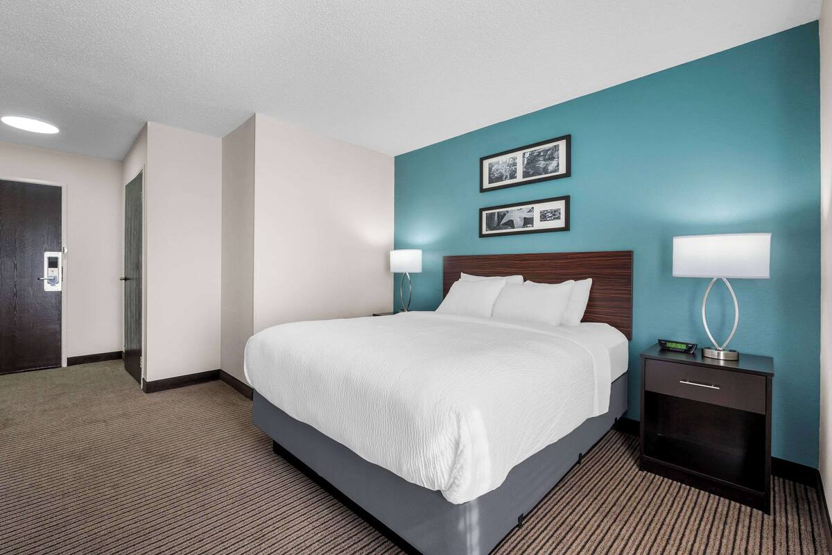 A hotel room with a large bed, two bedside tables with lamps, and a door leading to another room.