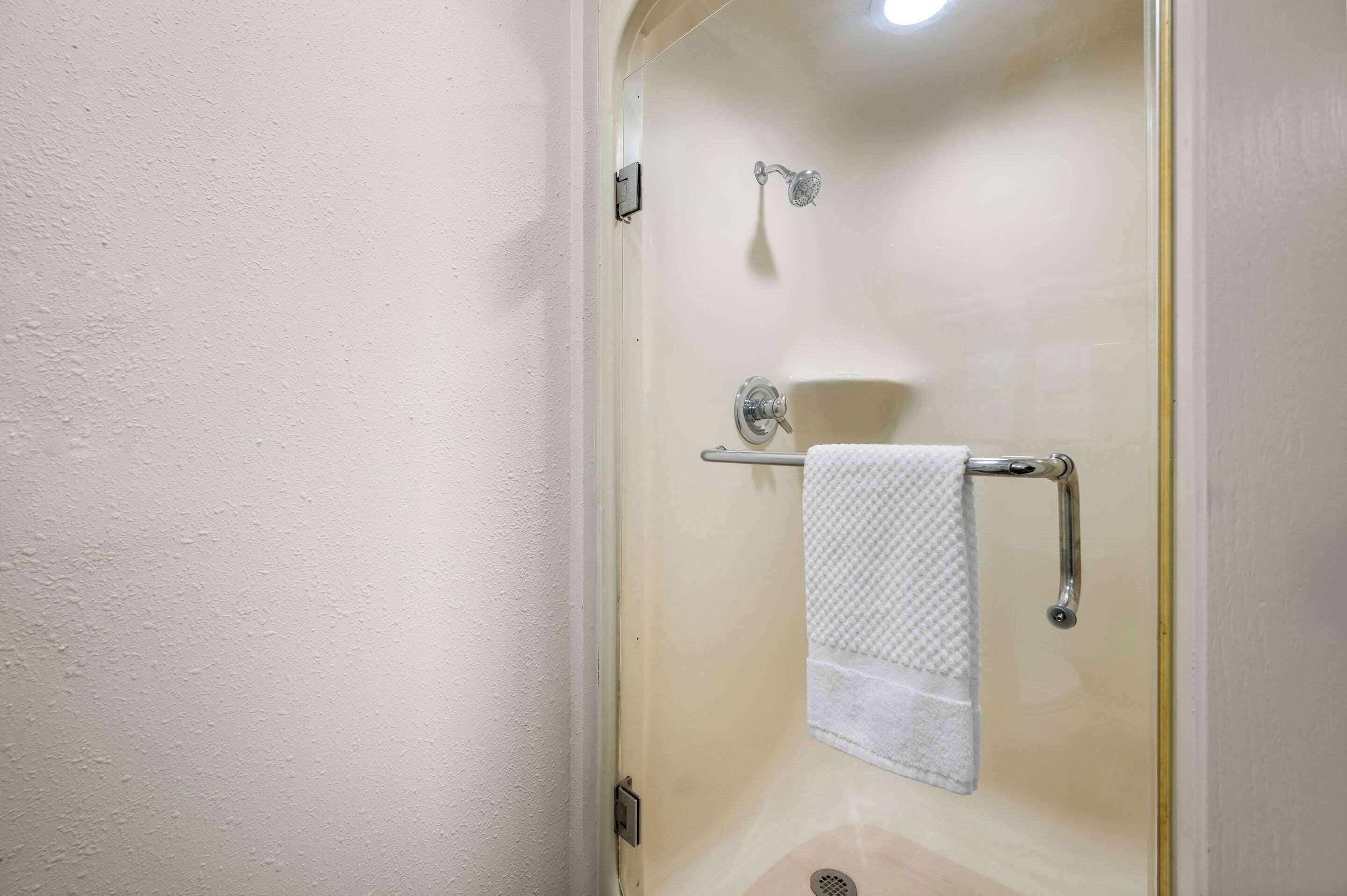 Um chuveiro com divisória de vidro, um porta-toalhas com uma toalha dobrada e um ralo visível.