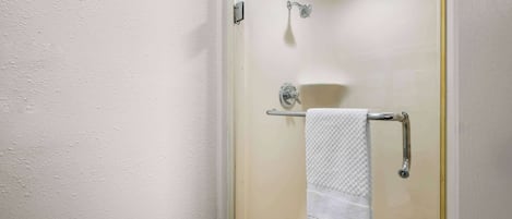 A glass-enclosed shower with a handheld showerhead, a towel rack with a folded towel, and a visible drain.