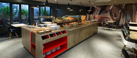 A modern restaurant with a central counter, red shelving, and a mural on the wall.