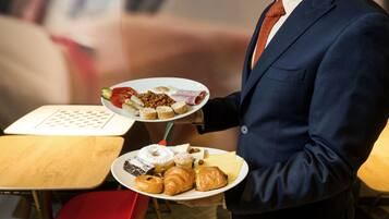 A person holding two plates of food, one with pastries and the other with a variety of items including bread and vegetables.