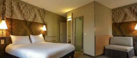 Una habitación de hotel con cama, mesitas de noche, una silla y una puerta que da a un baño.
