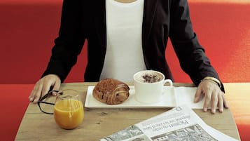 Uma pessoa sentada à mesa com um croissant, uma xícara de café e um copo de suco de laranja.